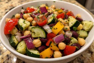 A vibrant, close-up view of a high protein bean salad featuring chickpeas, kidney beans, cucumbers, red onion, and bell peppers in a white bowl.