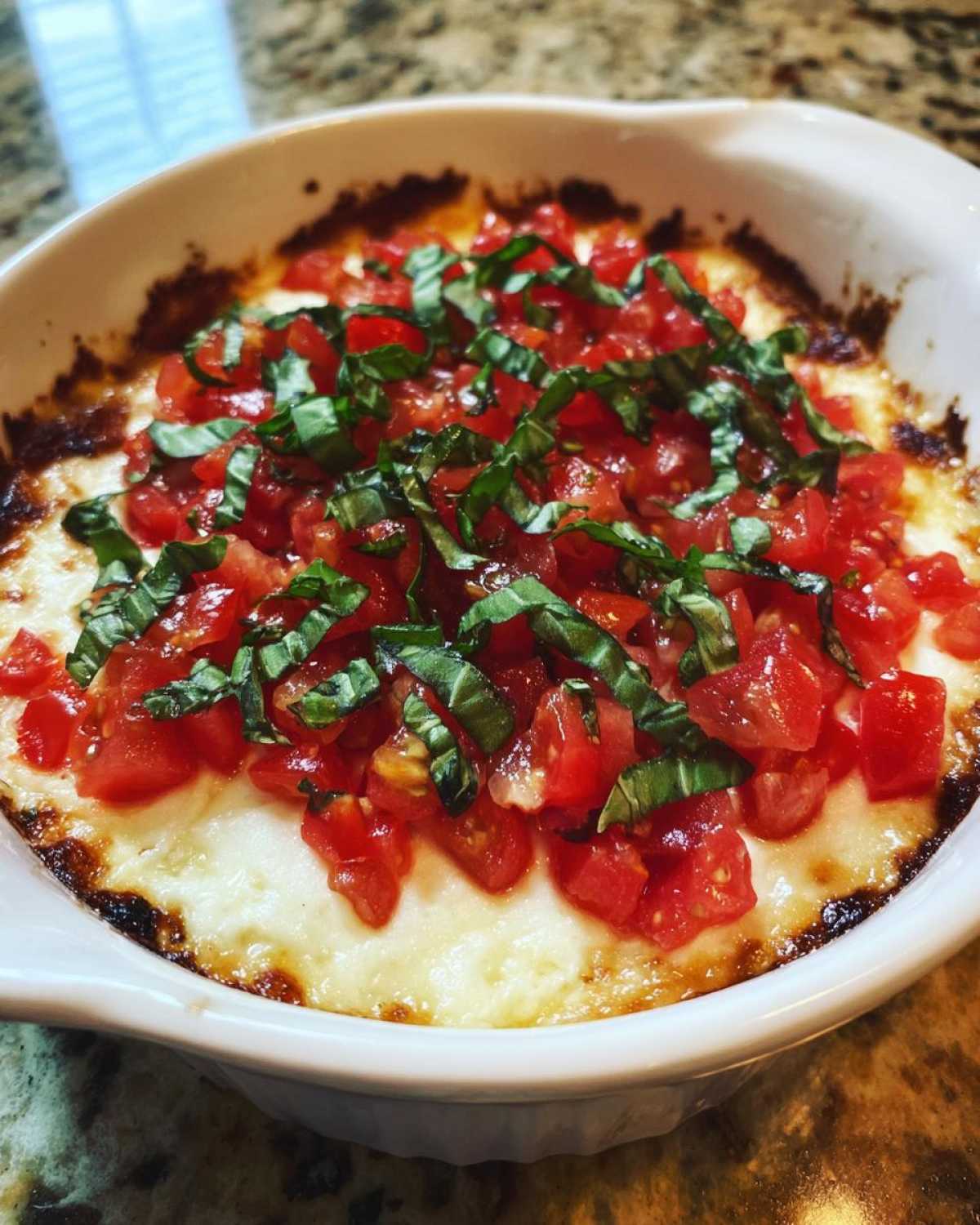 Close-up of a hot 3-cheese bruschetta dip, featuring melted cheese topped with diced tomatoes and fresh basil.