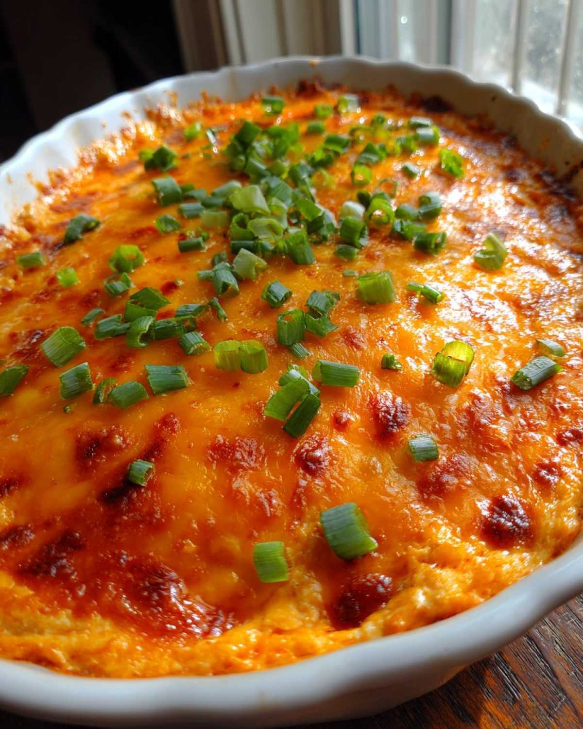 Close-up of hot, bubbly Buffalo chicken dip topped with melted orange cheddar cheese and fresh green onions.