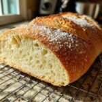 Cross-section of freshly baked Italian bread showing an open, airy crumb structure resting on a cooling rack.