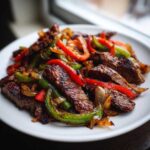 Close-up of juicy steak fajitas featuring seared steak strips mixed with caramelized onions and vibrant red and green bell peppers.