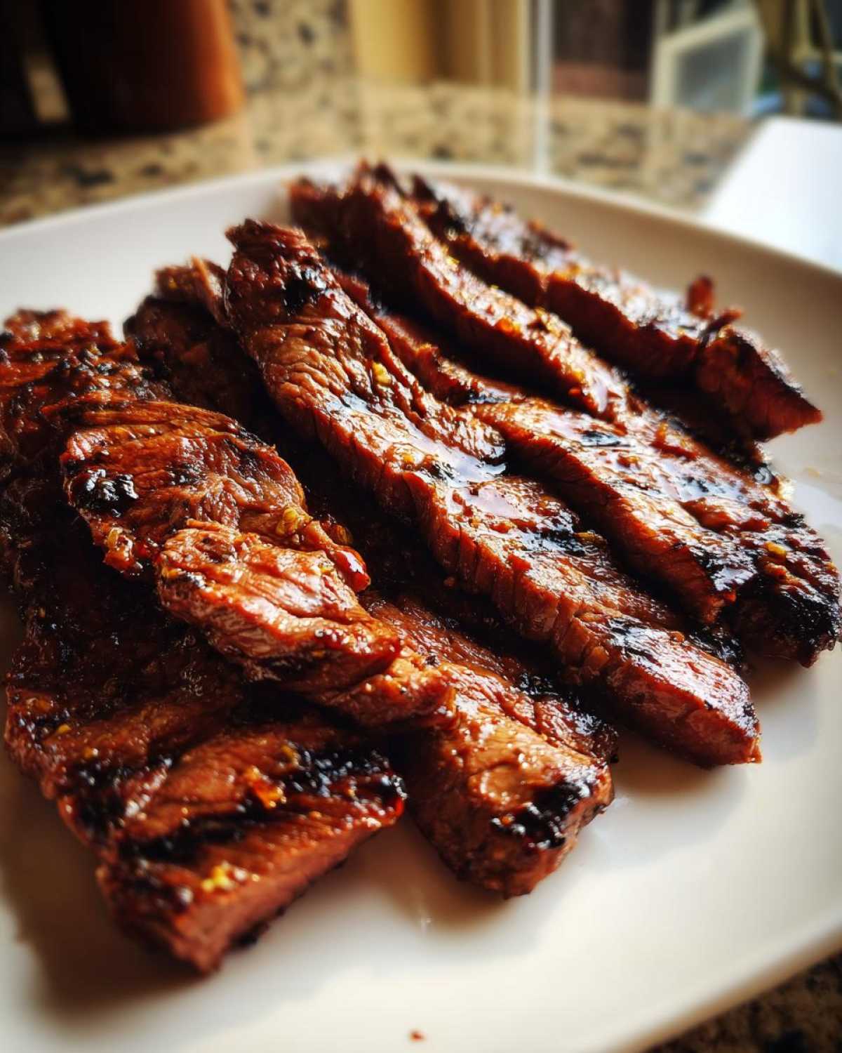 Close-up of perfectly grilled and sliced steak coated in a glistening Carne asada marinade, resting on a white plate.