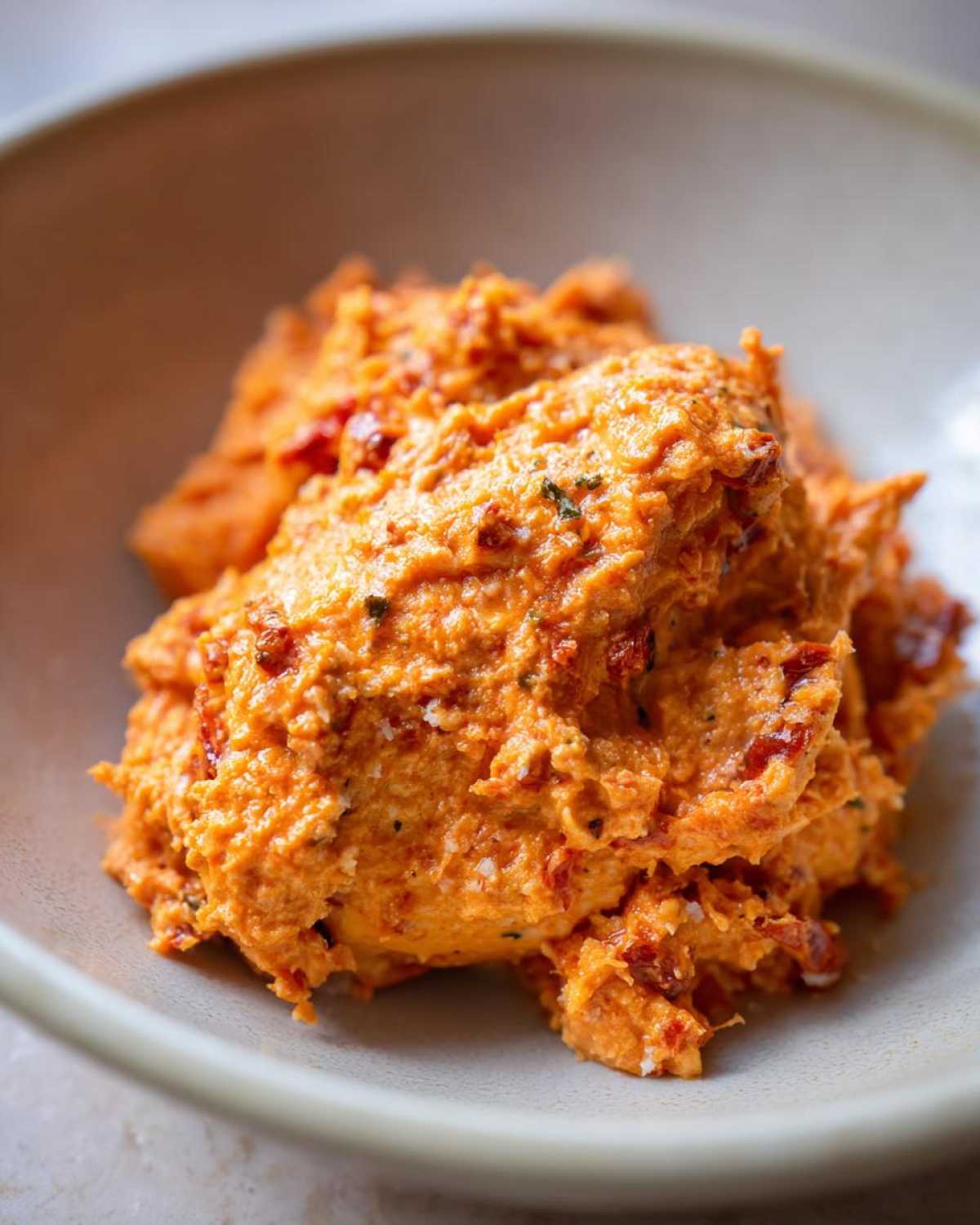 Close-up of creamy, orange-red sun-dried tomato sauce, likely for Marry Me Chicken, in a light bowl.