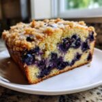 A thick slice of moist blueberry banana bread topped with streusel and a light glaze.