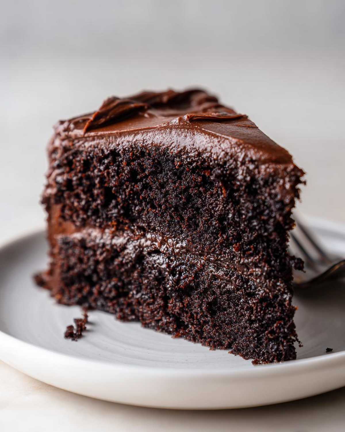 Close-up of a moist slice of rich chocolate fudge cake with thick, glossy frosting.
