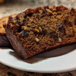 Close-up of a thick, moist slice of date nut bread showing visible dates and walnuts inside.