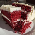 Close-up of a thick slice of vibrant red velvet cake layered with white cream cheese frosting.