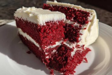 Close-up of a thick slice of vibrant red velvet cake layered with white cream cheese frosting.