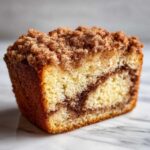 Close-up of a moist slice of sour cream coffee cake showing a cinnamon swirl and thick, crumbly topping.