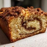 Close-up of a moist slice of sour cream coffee cake showing a cinnamon swirl and thick crumb topping.