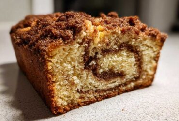 Close-up of a moist slice of sour cream coffee cake showing a cinnamon swirl and thick crumb topping.