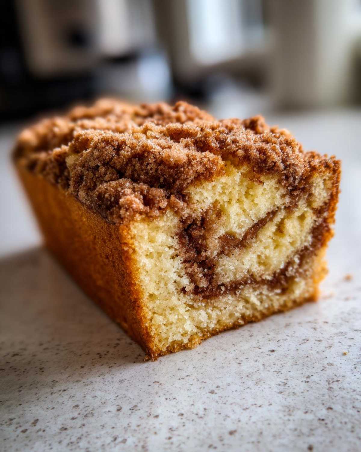 Close-up of a moist slice of sour cream coffee cake showing a cinnamon swirl and thick crumbly streusel topping.