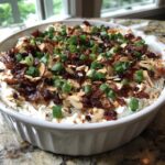 Close-up of creamy Neiman Marcus Dip topped generously with crumbled bacon, sliced almonds, and chopped green onions.