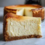 A close-up, appetizing slice of rich New York cheesecake showing the creamy texture and thick graham cracker crust.