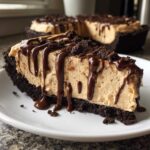 A thick slice of no-bake peanut butter pie with a dark chocolate crust, topped with chocolate syrup drizzle and crumbs.