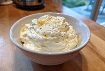 A close-up of thick, creamy Olive Garden Alfredo Sauce topped with black pepper in a white bowl.