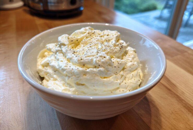 A close-up of thick, creamy Olive Garden Alfredo Sauce topped with black pepper in a white bowl.