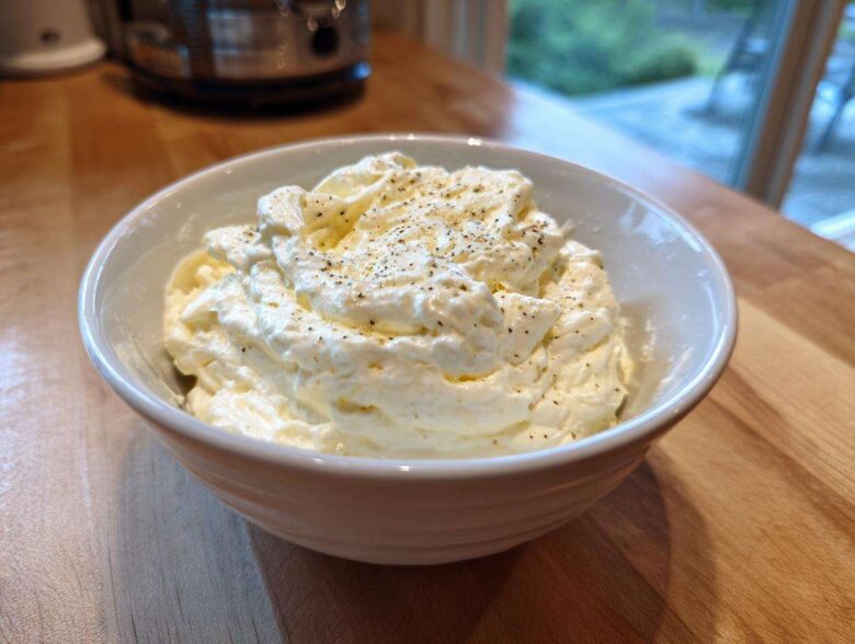 A close-up of thick, creamy Olive Garden Alfredo Sauce topped with black pepper in a white bowl.