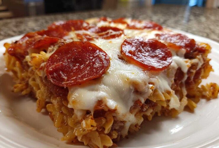 A close-up of a serving of baked pizza pasta, topped with melted mozzarella and pepperoni slices.
