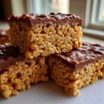 Close-up of stacked peanut butter rice krispie treats topped with a thick layer of melted chocolate.