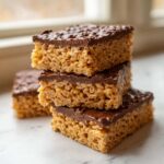 A stack of four homemade peanut butter rice krispie treats topped with a layer of melted chocolate.