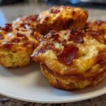 Close-up of several golden-brown Pizza Muffins topped with melted cheese and crispy pepperoni pieces, served on a white plate.