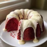 A vibrant red velvet bundt cake, partially sliced, generously covered in dripping white cream cheese glaze.