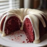 A rich, deep red velvet bundt cake, sliced open and drizzled generously with white cream cheese glaze.
