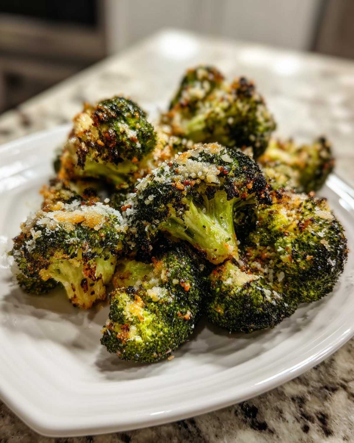 Close-up of perfectly roasted broccoli florets sprinkled with grated Parmesan cheese on a white plate.