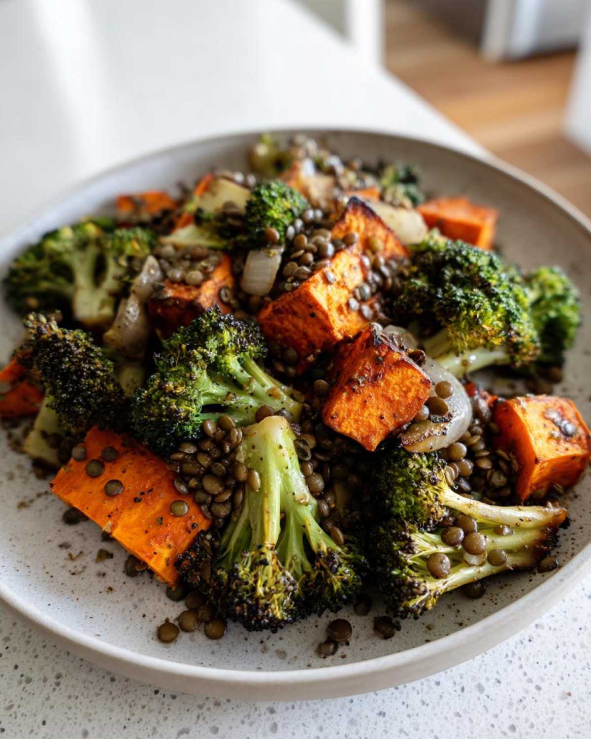 Close-up of roasted sweet potatoes, broccoli florets, and brown lentils making up a hearty veggie lentil salad.