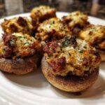 Close-up of several baked Sausage stuffed mushrooms topped with browned filling and fresh parsley on a white plate.