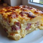 A square portion of cheesy scalloped potatoes and ham bites with a golden, bubbly top crust.