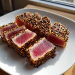 Slices of perfectly seared ahi tuna coated in a sesame seed crust, showing a bright pink center.