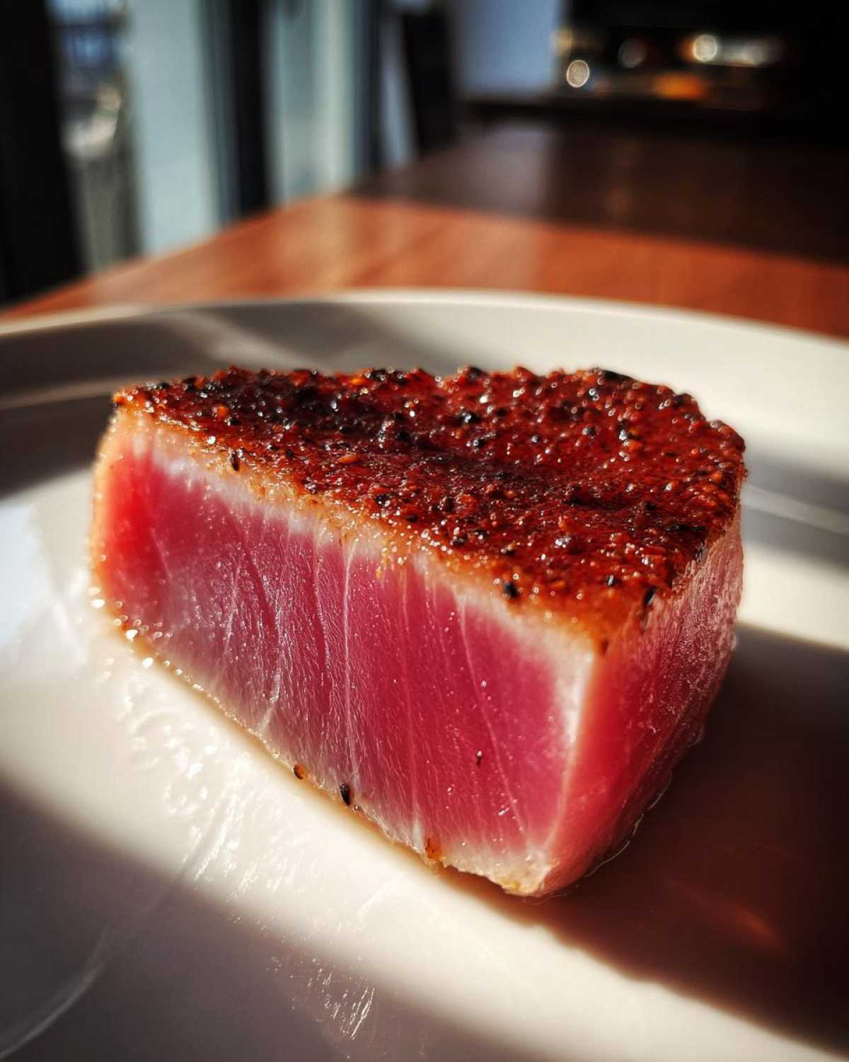 Close-up of a perfectly seared tuna steak, rare in the center, seasoned and resting on a white plate.