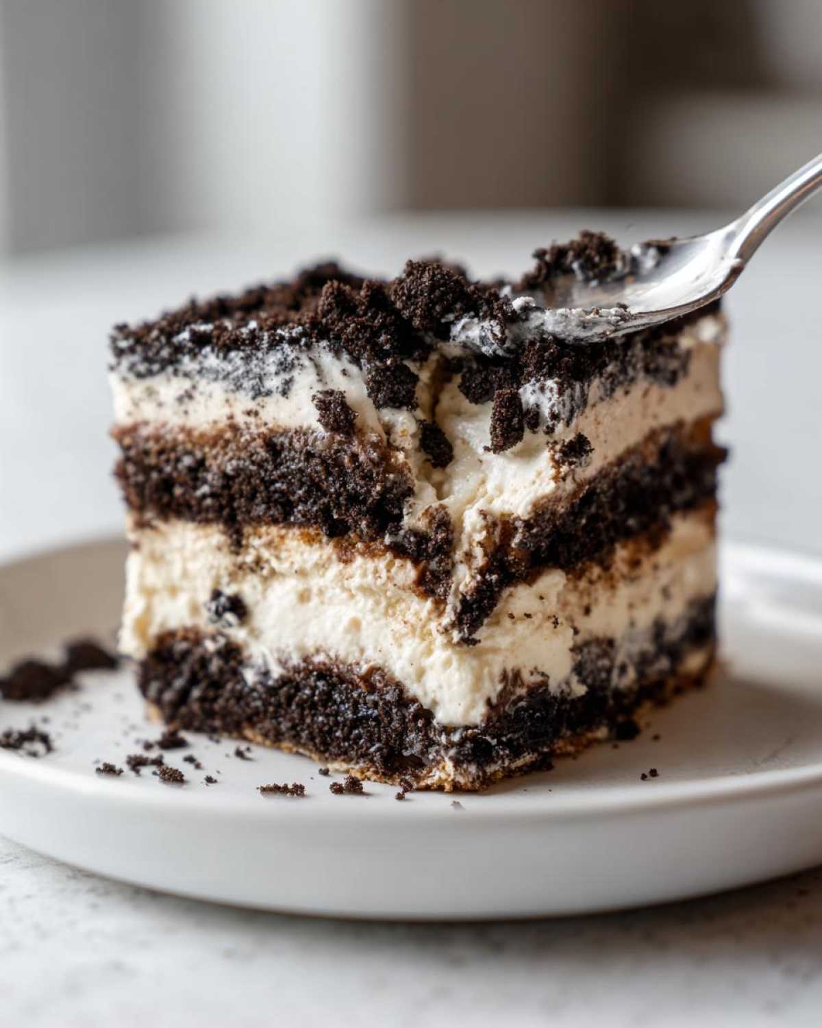 A fork taking a bite out of a layered slice of amazing oreo dirt cake with cream filling and cookie crumbs.