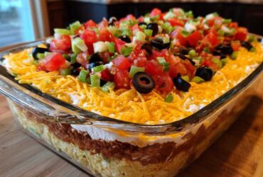 Close-up of a vibrant Seven layer dip topped with shredded cheese, tomatoes, olives, and green onions.
