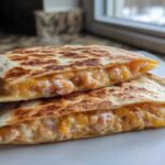 Two halves of a golden-brown shrimp quesadilla stacked, showing melted cheese and pink shrimp filling.