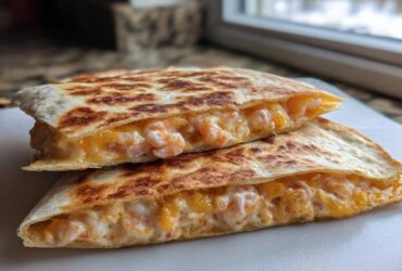 Two halves of a golden-brown shrimp quesadilla stacked, showing melted cheese and pink shrimp filling.