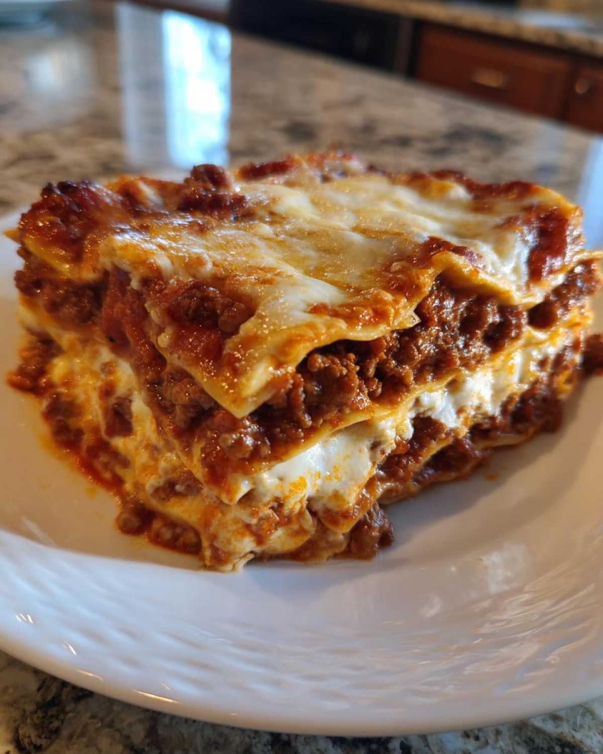 A generous, layered slice of homemade lasagna featuring rich meat sauce and melted cheese topping on a white plate.