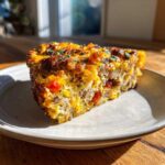 A hearty slice of savory egg bake featuring sausage, cheese, and peppers, garnished with herbs.