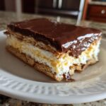 A single serving slice of layered eclair cake featuring graham crackers, vanilla pudding, and a glossy chocolate topping.