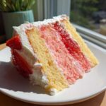 A delicious slice of strawberry cake featuring layers of yellow and pink sponge, strawberry filling, and white cream frosting.