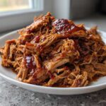 A generous serving of saucy, shredded Slow cooker pulled pork piled high on a white plate.