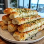 A tall stack of golden brown, soft buttery breadsticks topped with melted cheese, parsley, and Parmesan.