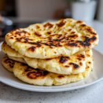 A stack of four freshly cooked homemade naan bread rounds with beautiful golden-brown spots and charring.
