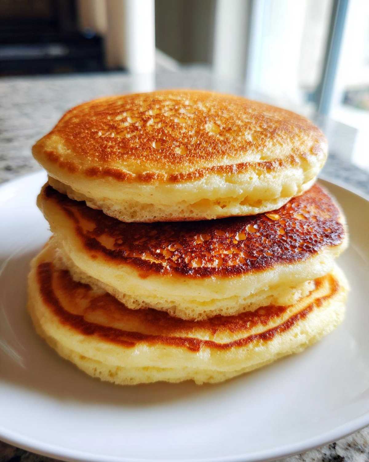 A close-up stack of three incredibly fluffy pancakes showing their golden-brown, perfectly cooked tops.