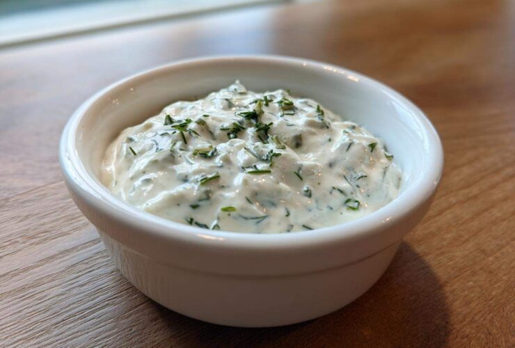 Close-up of creamy homemade tartar sauce recipe topped with fresh chopped herbs in a small white bowl.