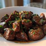 A white bowl filled with tender, saucy crockpot steak bites topped generously with fresh chopped parsley.