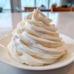 A tall, perfectly piped swirl of creamy white vanilla buttercream frosting on a small white dish.
