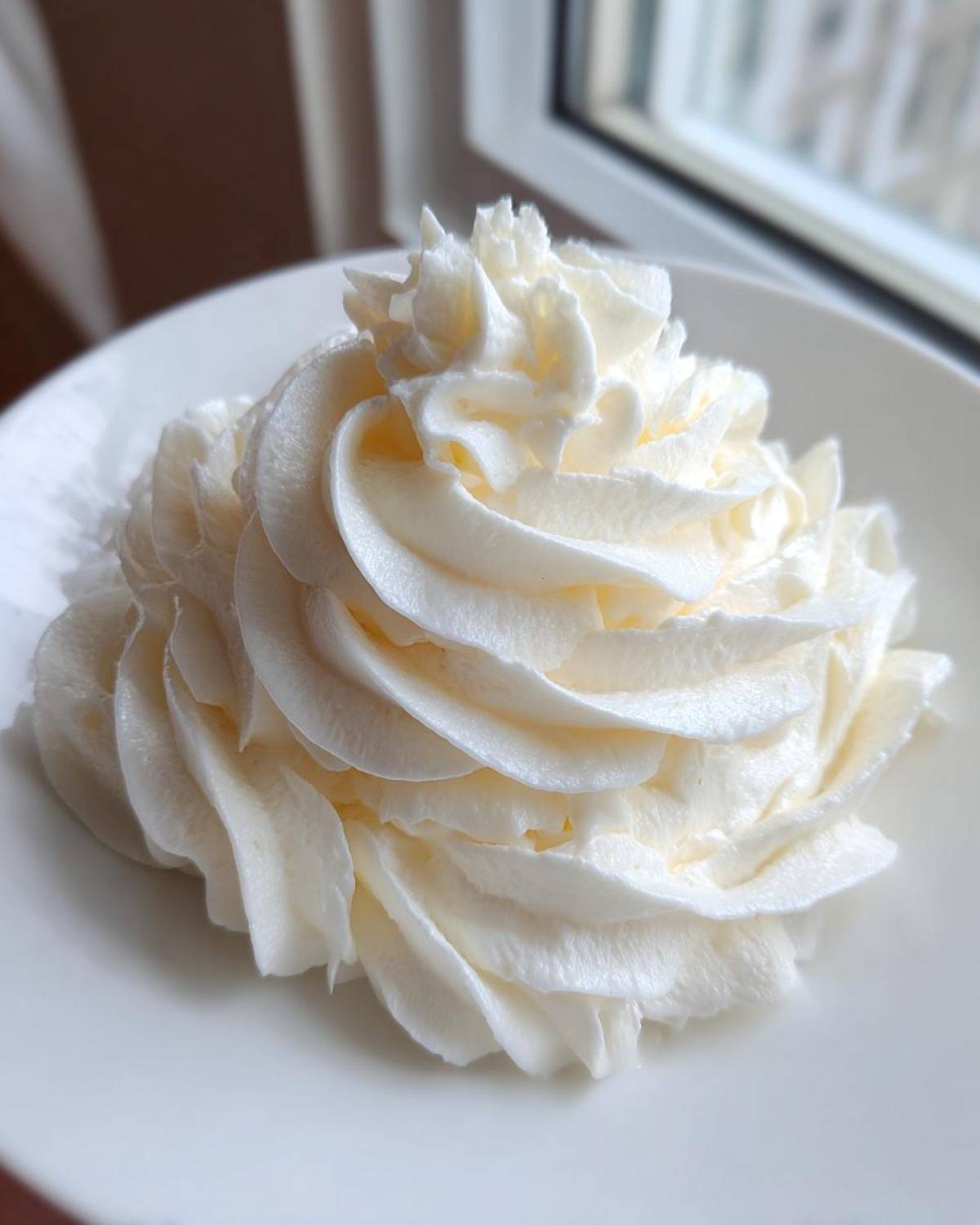 A beautiful, stiff swirl of creamy white vanilla buttercream frosting piped onto a white plate.